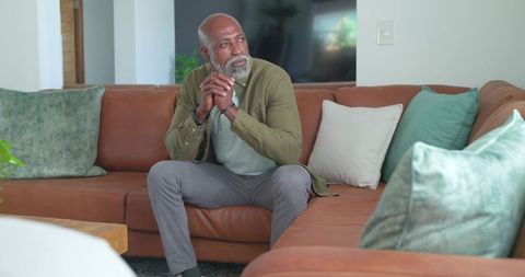 Senior african man sitting on leather sofa contemplating life in modern living room