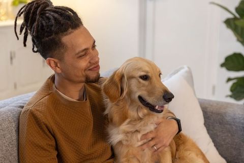 Relaxing man cuddling golden retriever on sofa in cozy living room