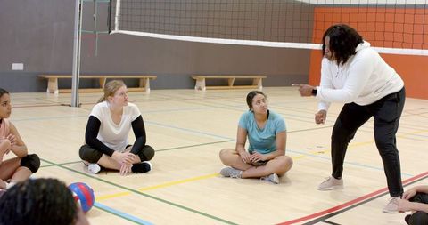 African american coach leading women's volleyball players in gymnasium coaching teamwork