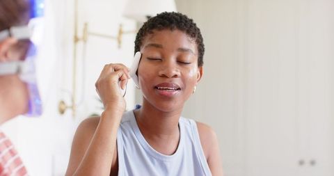 African american woman using facial device, enjoying self-care routine and glowing skin