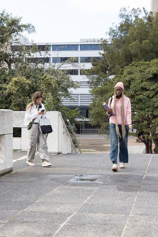 Diverse female students walking across university plaza using smartphones and notebooks