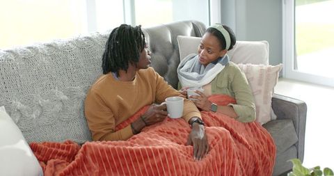 African American Couple Snuggling on Sofa Sharing Coffee and Talking Under Warm Blanket