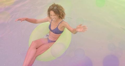 Woman floating on lime green swim ring in navy bikini smiling and splashing on calm water