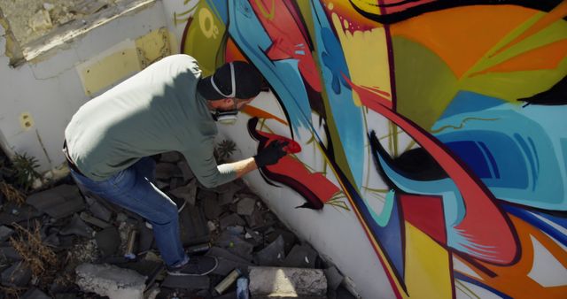 Image shows a street artist spray painting a mural with vibrant colors on an urban wall. Ideal for use in articles about contemporary art, street culture, urban creativity, and public art initiatives. Can be used for marketing campaigns promoting artistic freedom, community art projects, or advertisements for art supplies.