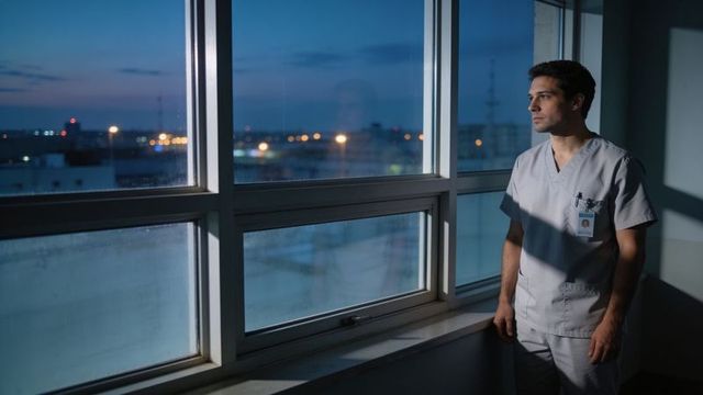Clinician gazing out at city twilight from hospital window, contemplative healthcare moment