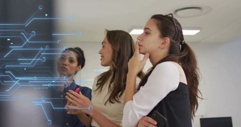 Three professional women reviewing futuristic digital interface on office glass display