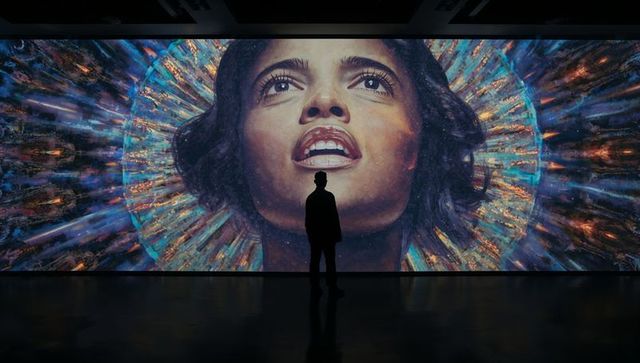 Silhouette visitor standing before radiant halo mural portrait in dark gallery with reflection