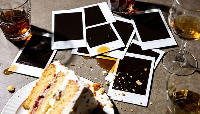 Polaroids lying stained on stone table with cake crumbs, spilled drink and glasses