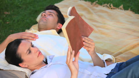 Couple Relaxing Outdoors While Reading and Resting on Blanket