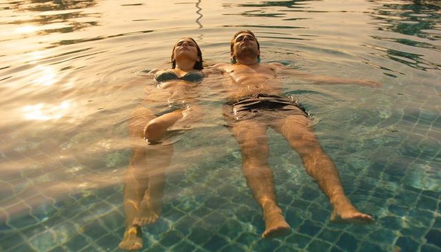 Sunlit couple floating side-by-side in pool at resort during golden hour relaxing together