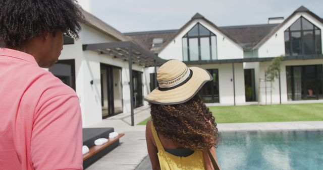 A couple enjoys a serene setting at a modern luxury house with a pool on a summer day. Perfect for use in advertisements for vacation rentals, real estate promos, summer clothing lines, or lifestyle blogs.
