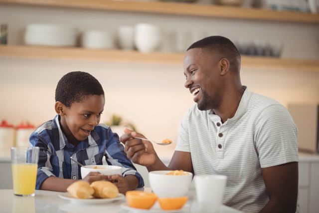 Father and son sharing a joyful moment while having breakfast in a modern kitchen. Perfect for promoting family values, parenting tips, breakfast foods, or home lifestyle content.