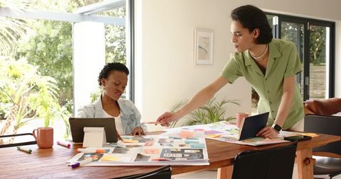 Multiracial designers collaborating on creative moodboard and tablet in bright home studio