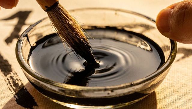 Calligraphy brush dipping into ink creating concentric ripples in glass ink dish sumi-e