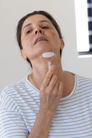 Mature woman using rose quartz facial roller on neck during morning skincare routine