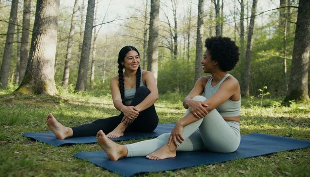 Smiling women practicing yoga together on mats in peaceful forest clearing