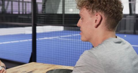 Friends chatting by indoor padel court holding coffee and racket