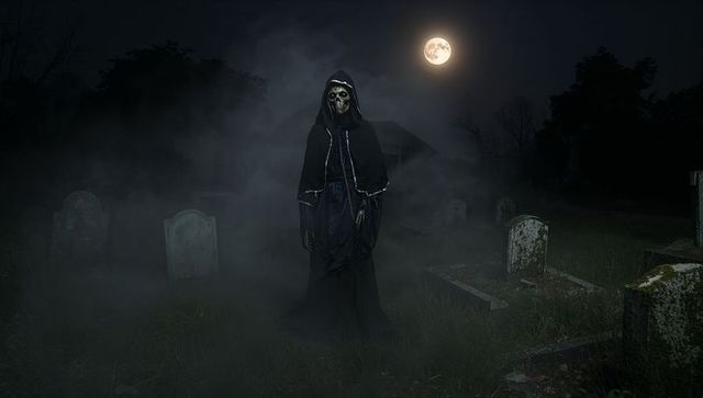 Skeletal figure in black cloak haunting moonlit cemetery