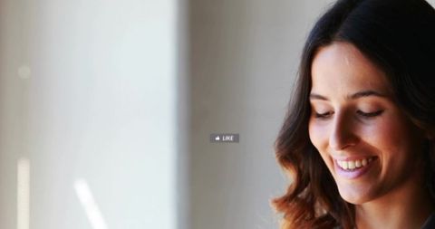Smiling white woman looking down by window with like icon overlay and soft natural light