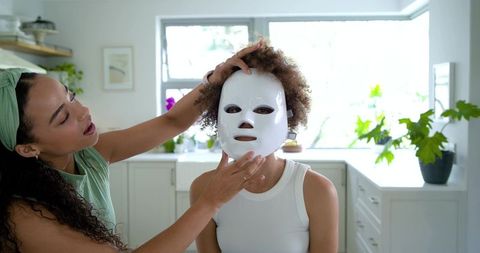 African american women adjusting led facial mask home skincare routine in bright kitchen
