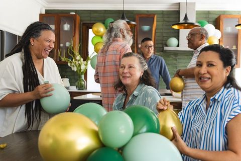 Multigenerational friends preparing green and gold balloon decorations in cozy kitchen