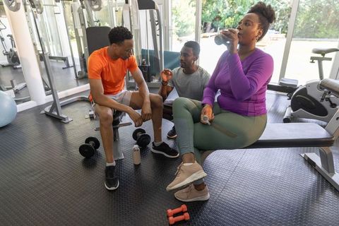 African american friends resting, hydrating and chatting after gym workout on bench
