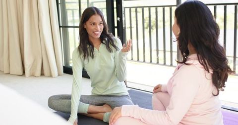 Diverse women practicing yoga and chatting on sunlit balcony mats for wellness