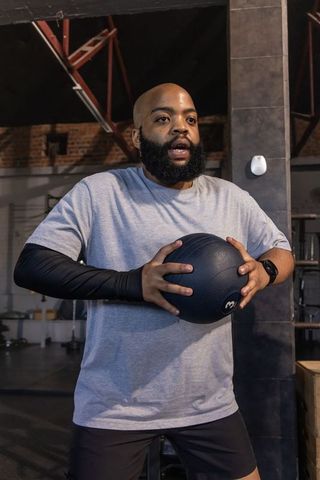 African american man holding medicine ball training in warehouse gym compression sleeve