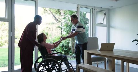 Senior woman in wheelchair with caregiver and husband at home