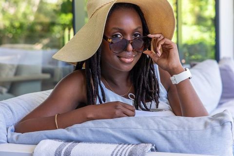 Stylish woman reclining on sunroom sofa wearing straw hat and sunglasses summer lounge