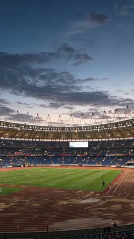 Vertical stadium video showing floodlit empty running track and green pitch under dusk sky