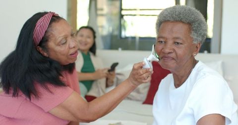 Senior woman receiving cheek temperature at home by caregiver using digital thermometer