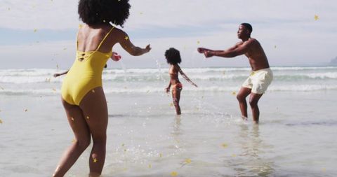 Family splashing and playing on sunny beach with golden star confetti and bright swimwear