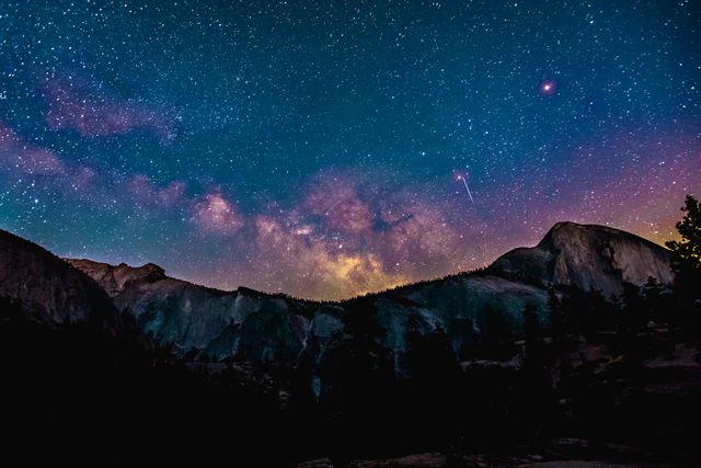 Milky Way stretching across star-filled sky over peaks and silhouettes of mountains. Ideal for astronomy blogs, nature articles, travel brochures, and background images for apps or websites emphasizing natural beauty or nighttime scenery.