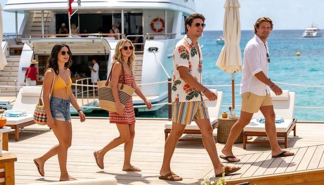 Four friends walking on luxury marina dock in summer resortwear with white yacht backdrop