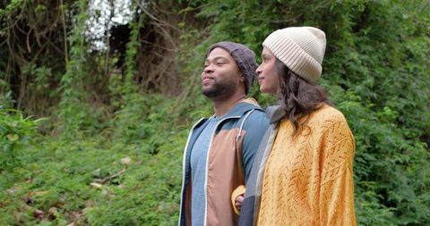 Autumn stroll: diverse couple wearing knit beanies and layered fall look on forest trail
