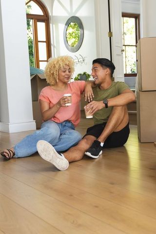 Young couple unpacking boxes sharing coffee on new home hardwood floor moving day joy
