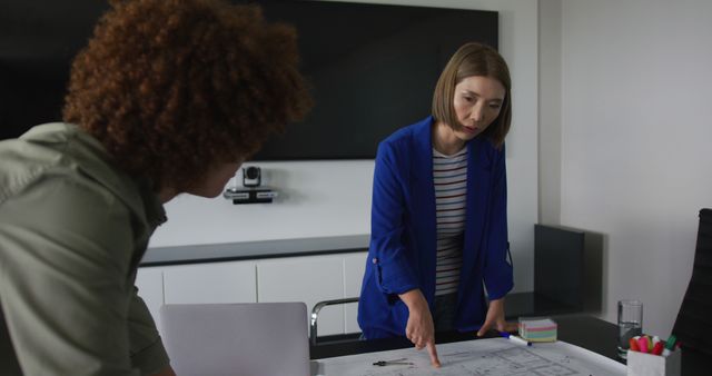 Female architect in a blue blazer explaining architectural plans to a colleague in a modern office. Could be used for business, architecture, teamwork, or office environment concepts. Ideal for promoting collaboration, innovation, and professional services in both digital and print media.