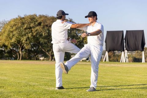 Cricket players stretching on grass before match performing partner balance drills in white kits