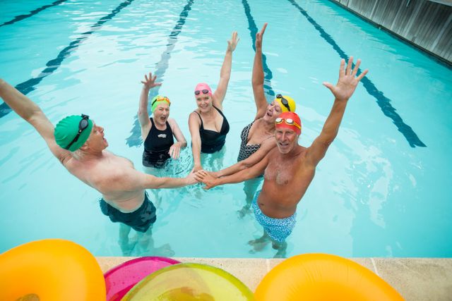Group of active seniors enjoying time together in a swimming pool, stacking hands in a show of unity and teamwork. Ideal for promoting senior fitness, healthy lifestyles, and social activities for the elderly. Can be used in advertisements for senior wellness programs, aquatic exercise classes, and community centers.
