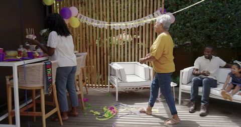 Senior woman walking across wooden deck toward seating at backyard birthday celebration