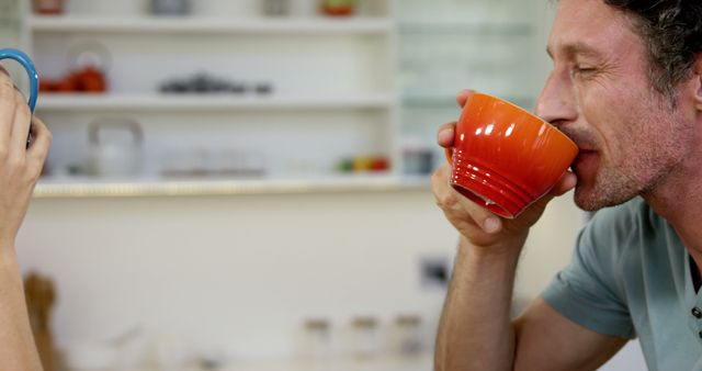 Man enjoying morning coffee in a modern kitchen, sipping from bright orange cup while smiling. Can be used to represent relaxation, daily routines, coffee time or breakfast moments in home environments.