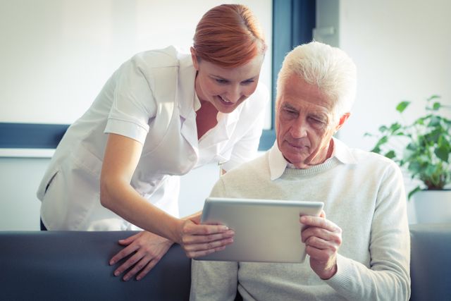 Nurse showing medical report to senior man on digital tablet. Ideal for use in healthcare, elderly care, and technology in medicine contexts. Can be used in articles, websites, and advertisements related to senior health, home care services, and medical consultations.
