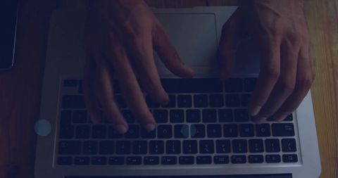 Typing adult male hands over silver laptop keyboard on wooden desk with phone and sticker
