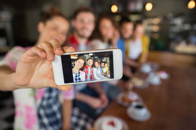 Group of friends taking a selfie in a pub, capturing a moment of fun and togetherness. Ideal for use in advertisements, social media campaigns, and articles about socializing, friendship, and modern lifestyle.