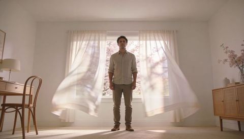 Man standing in sunlit minimalist room with sheer curtains and cherry blossom window view