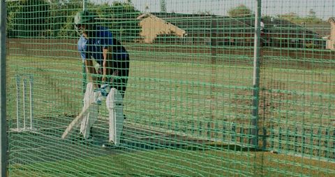 Cricket batsman practicing in outdoor net wearing helmet and pads during sunny training