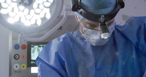 Surgeon in blue gown performing delicate surgery under led operating light with x-ray