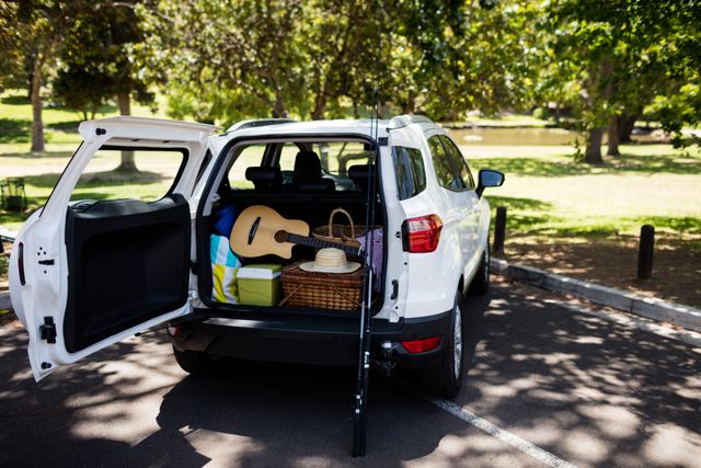 Car trunk packed with a guitar, fishing rod, and picnic basket, ready for an outdoor adventure on a sunny day. Ideal for promoting travel, leisure activities, family outings, and summer vacations. Perfect for use in advertisements, travel blogs, and lifestyle magazines.