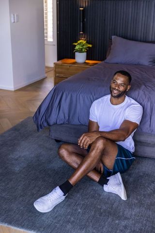 African american man sitting on bedroom rug relaxing in athletic shorts white sneakers